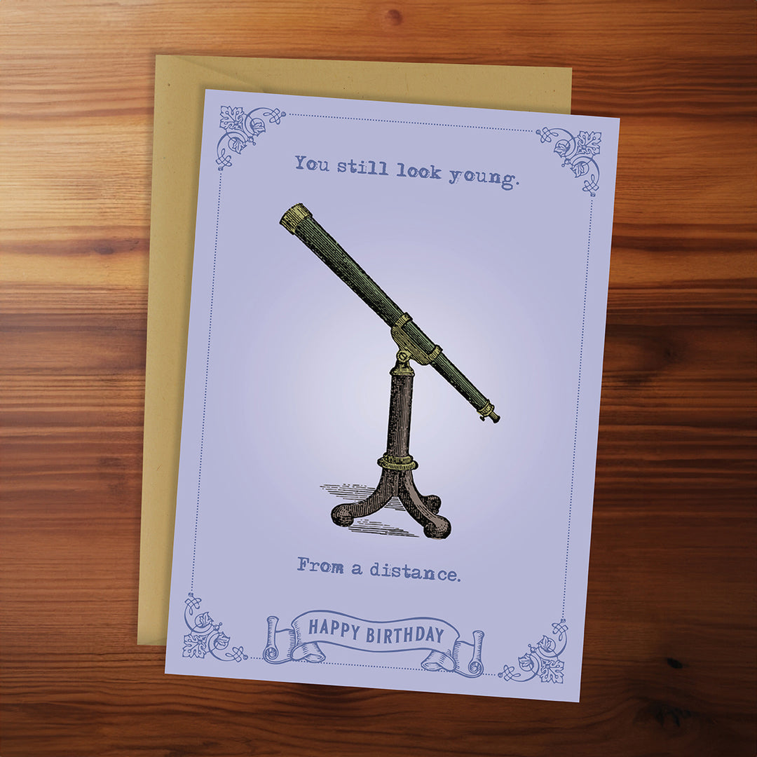 Greeting card with vintage telescope illustration and birthday message on a wooden surface