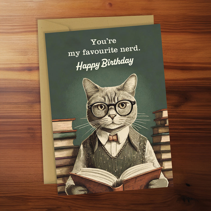 Birthday card with a cat wearing glasses and reading a book, on a wooden surface.
