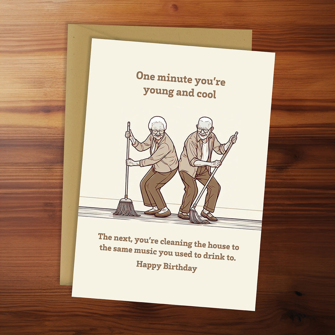 Birthday card with illustration of two older men cleaning and humorous text on a wooden surface