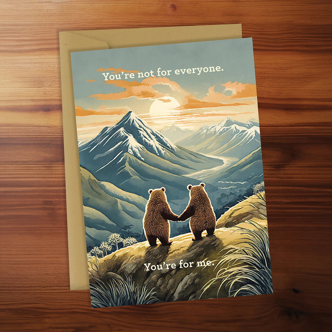 Greeting card with two bears holding hands and a mountain landscape on a wooden surface.