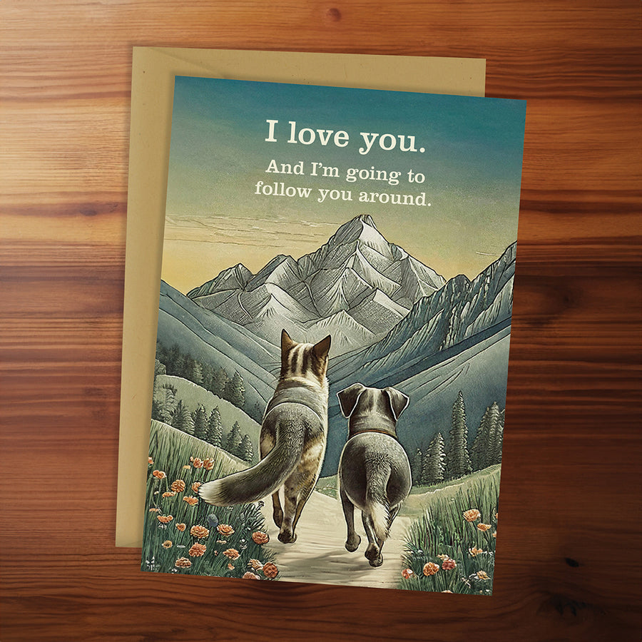 Greeting card with two animals walking together and a mountainous landscape, on a wooden surface.