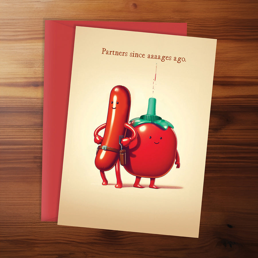 Card with cartoon sausage and tomato characters and humorous text on a wooden surface