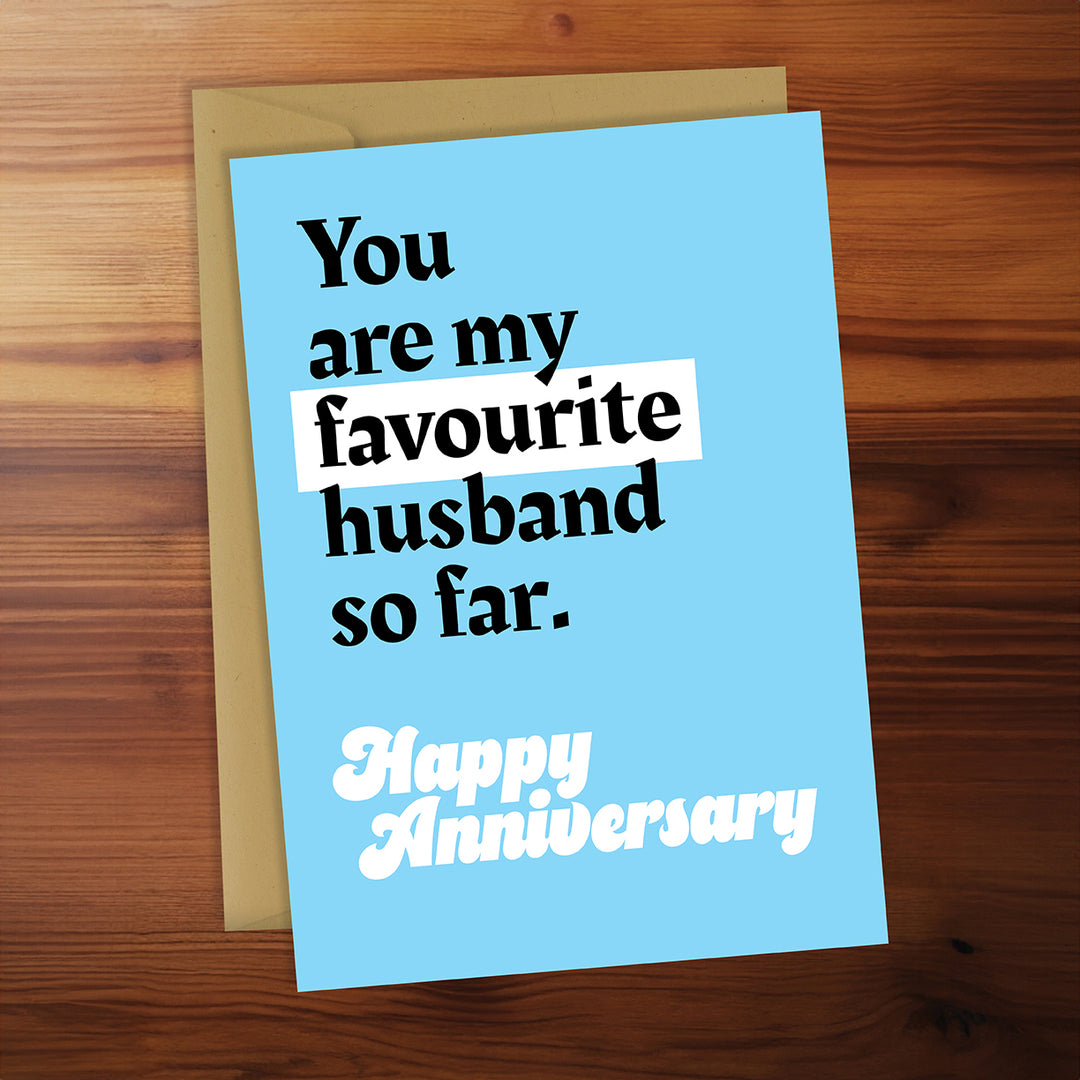 Greeting card with 'You are my favourite husband so far. Happy Anniversary' text on a wooden surface