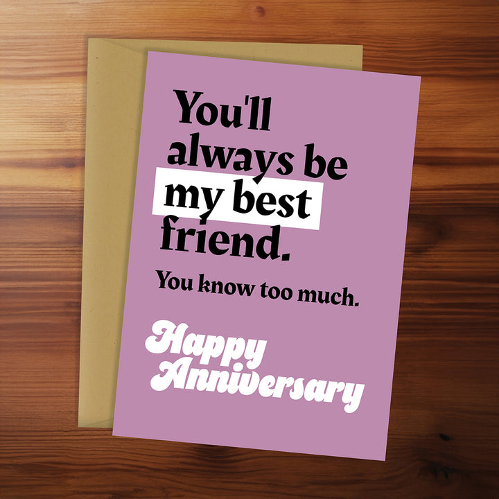 Pink anniversary card with humorous text on a wooden surface