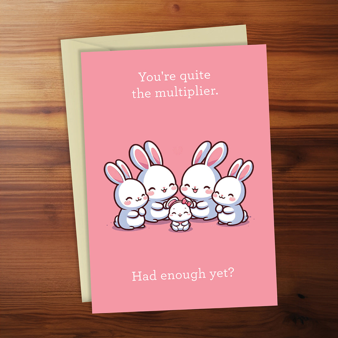 Pink card with cartoon bunnies and humorous text on a wooden surface