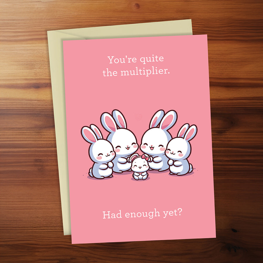 Pink card with cartoon bunnies and humorous text on a wooden surface