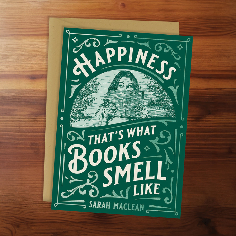 Green book with 'Happiness that's what books smell like' quote on a wooden surface