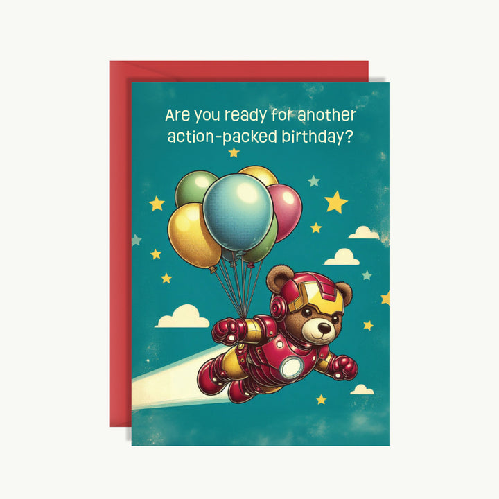Birthday card with a teddy bear in superhero costume flying with balloons against a blue sky.