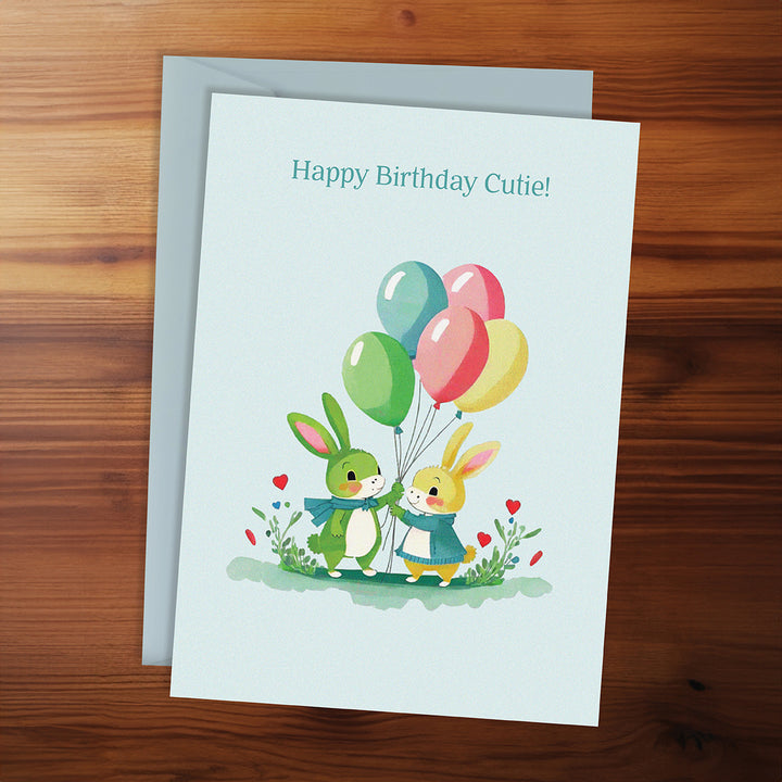 Birthday card with two bunnies holding balloons on a wooden surface