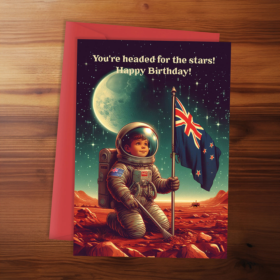 Birthday card with an astronaut on Mars holding a flag, featuring text 'You're headed for the stars! Happy Birthday!' on a wooden surface.