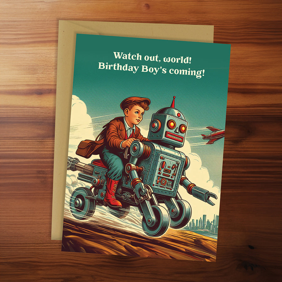Birthday card with a boy and robot on a motorcycle, text 'Watch out, world! Birthday Boy's coming!' on a wooden surface.