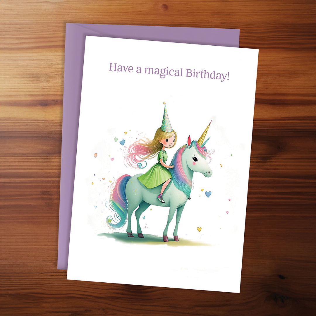 Greeting card with a girl riding a unicorn and 'Have a magical birthday!' text on a wooden surface.