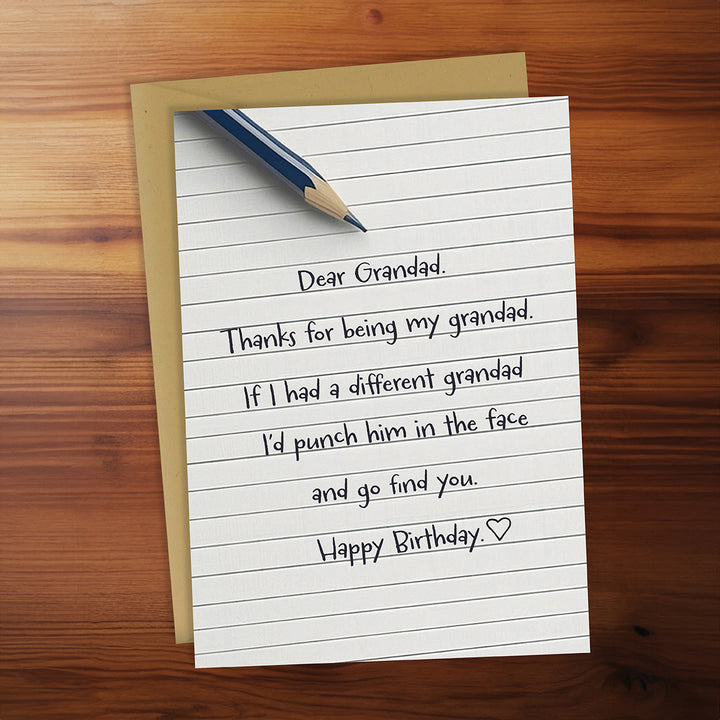 Note with humorous birthday message to grandad on lined paper with pencil, on wooden surface