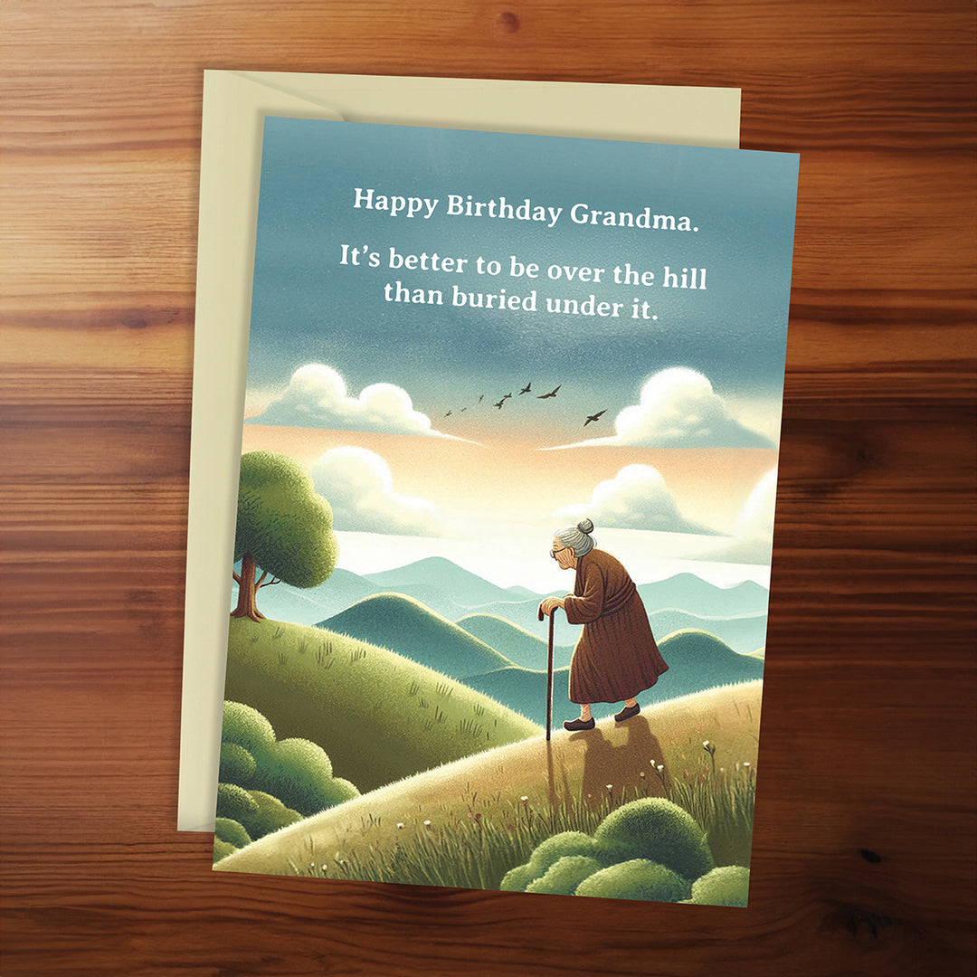 Birthday card for grandma with an illustration of a woman on a hill and humorous quote, on a wooden surface.