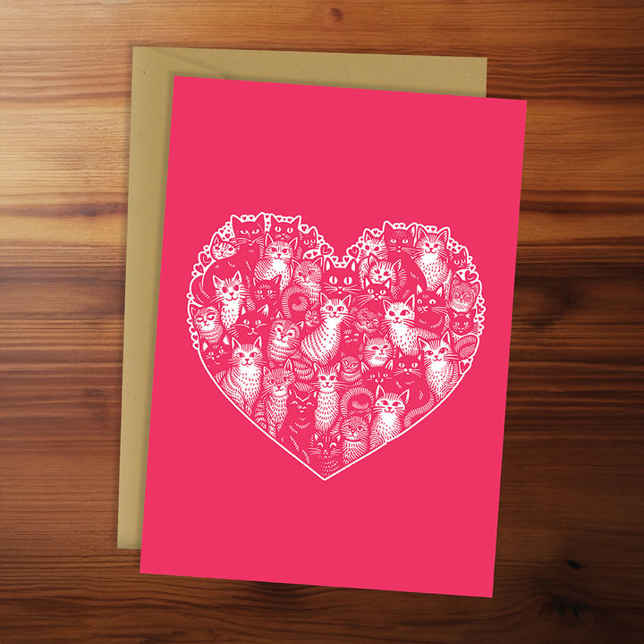 Pink card with white cat pattern in the shape of a heart on a wooden surface