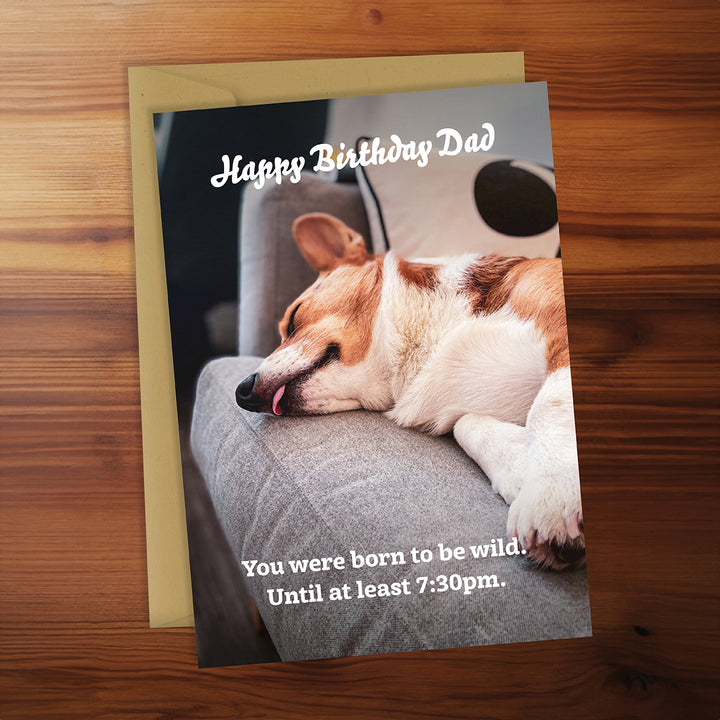 Birthday card with a dog on a chair and humorous text, placed on a wooden surface.