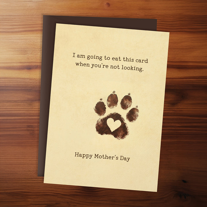 Card with paw print and humorous text on a wooden surface