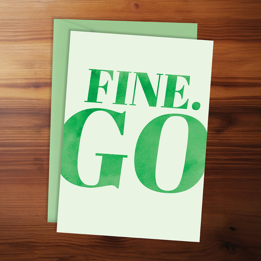 Green greeting card with 'FINE. GO' text on a wooden surface