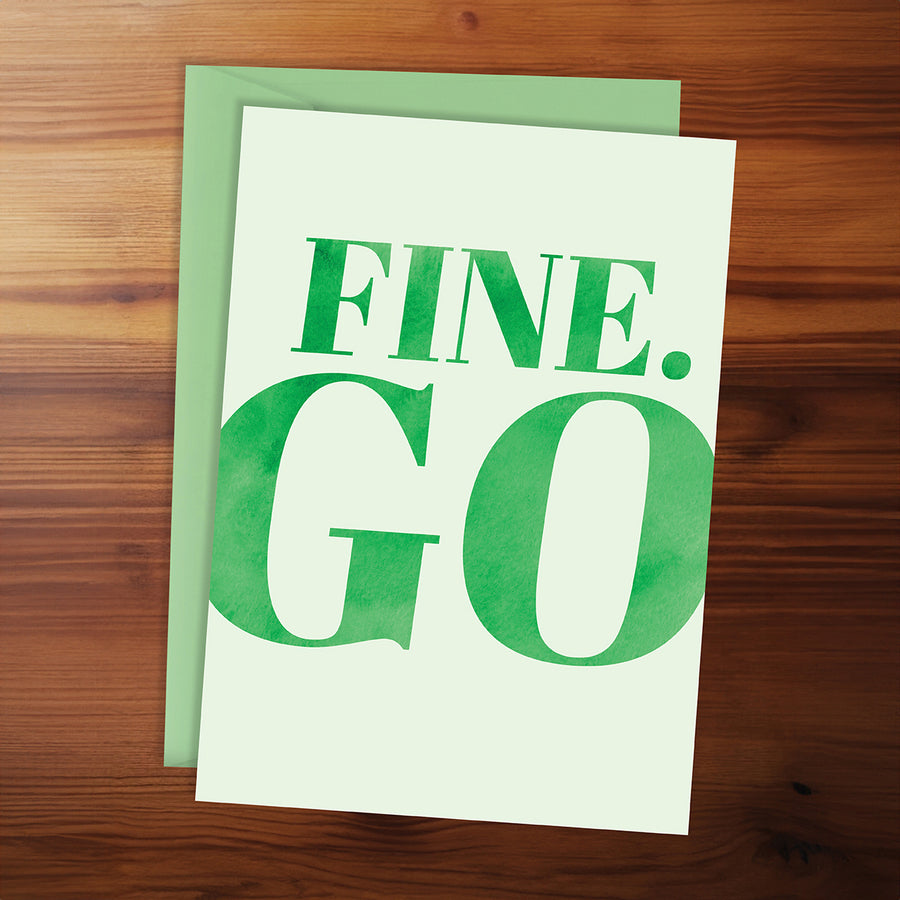 Green greeting card with 'FINE. GO' text on a wooden surface