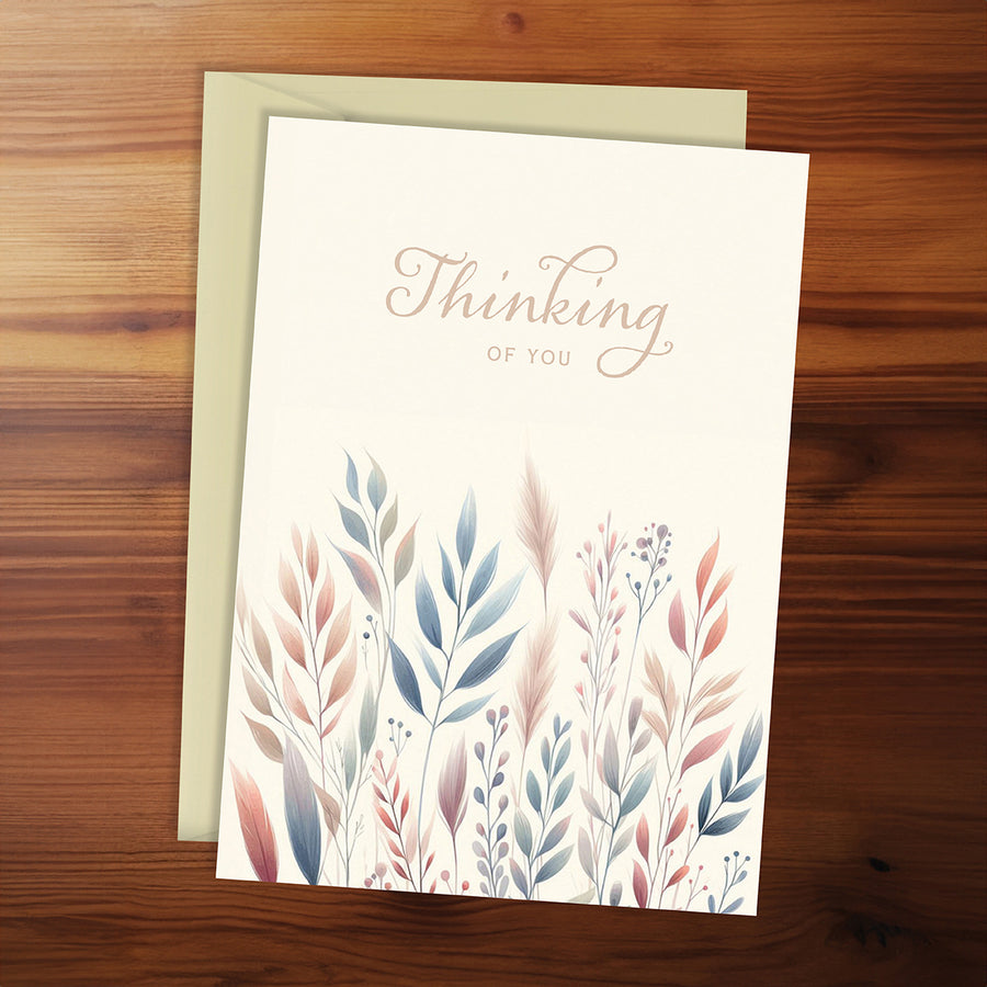 Greeting card with floral design and 'Thinking of You' text on a wooden surface