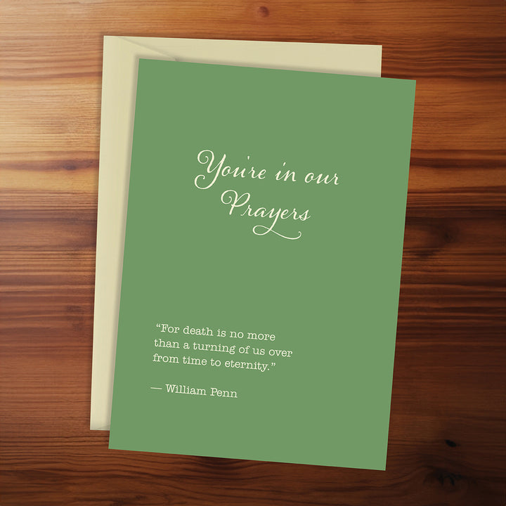 Green card with 'You're in our prayers' message on a wooden surface