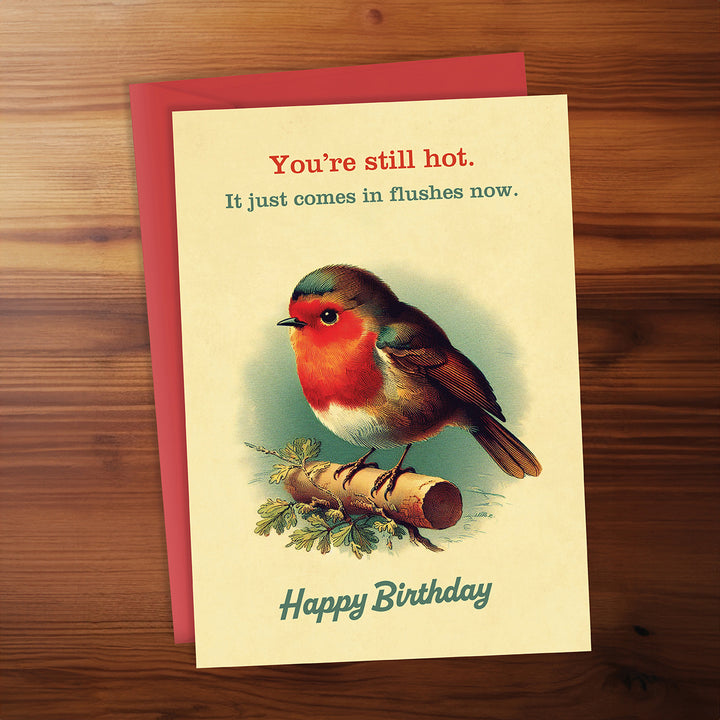 Birthday card with a robin illustration and humorous text on a wooden surface