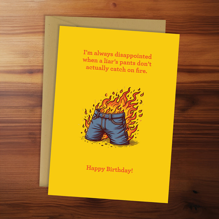 Birthday card with shorts on fire illustration and humorous text on a wooden surface