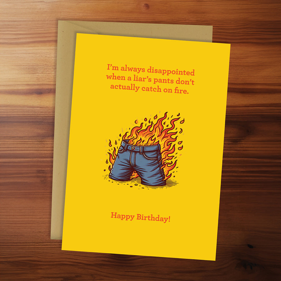 Birthday card with shorts on fire illustration and humorous text on a wooden surface