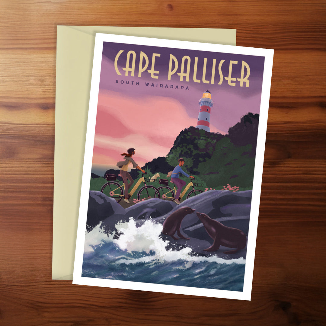 Cape Palliser greeting card with lighthouse, people on bikes, and seals on a wooden surface