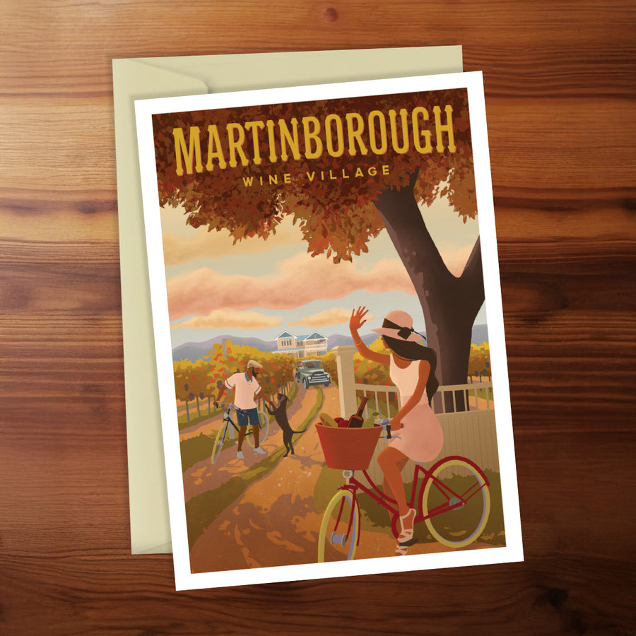 Poster of Martinborough Wine Village with a woman on a bike and a man with a dog, on a wooden surface.